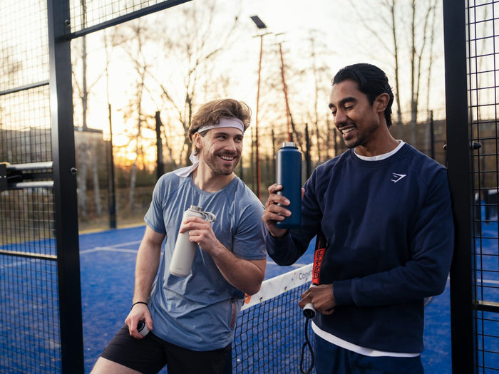 Two padel players laughing with their FLASKE bottles
