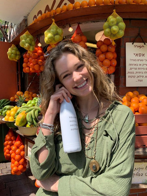 Woman at a fruit stall with a white FLASKE bottle