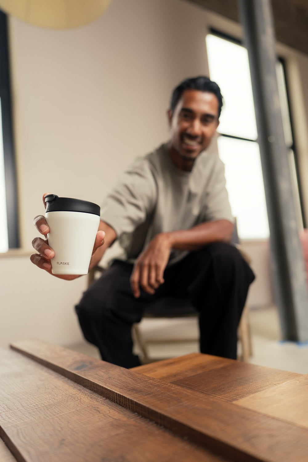 Man holding out his white FLASKE coffee cup