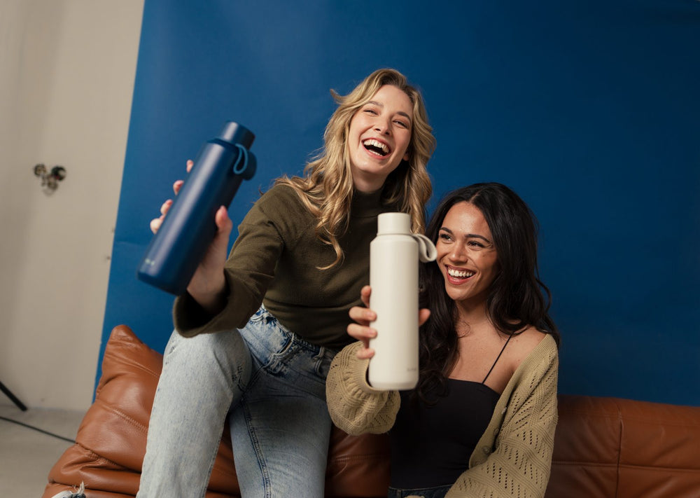 Two friends laughing on a sofa with FLASKE bottles