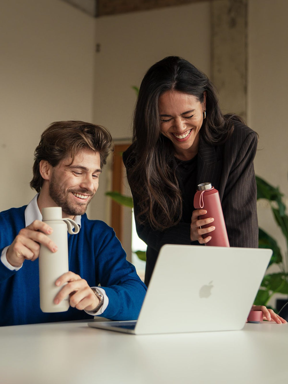 Two colleagues laughing at a laptop with FLASKE bottles