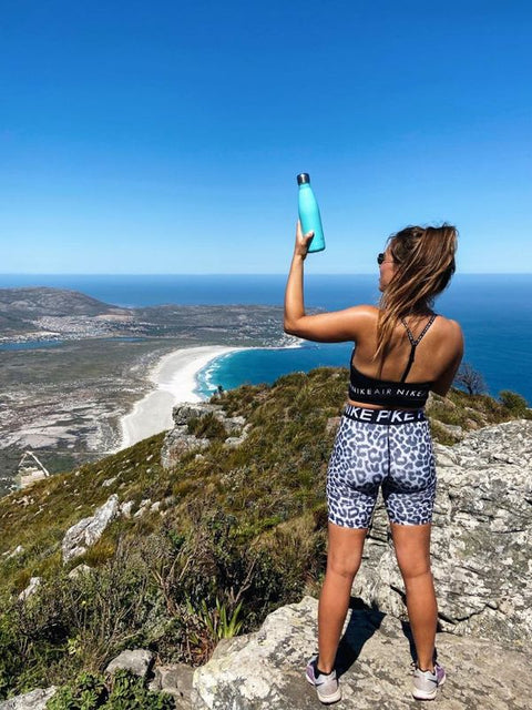 Hiker raising her FLASKE on a mountain top